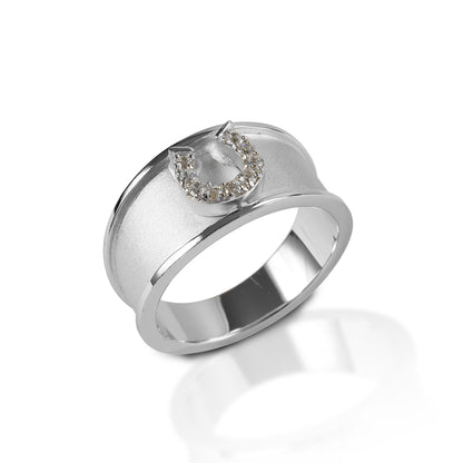 The Kelly Herd Wide Band Horseshoe Ring features a 9mm wide band of brushed sterling silver with a raised edge.  In the center sits a perfectly formed tiny horseshoe with pave cubic zirconia stones.  This ring is perfect for people who actually ride; no large single stones to catch on every piece of tack!   Features      Wide brushed band     Raised edge     Sterling silver     Clear cubic zirconia horseshoe