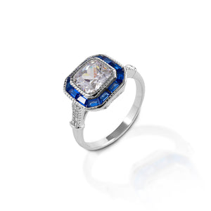 The Kelly Herd Small Asscher Cut/Blue Spinel Ring is just lovely! The modern asscher cut is similar to an emerald cut, but larger step facets, a higher crown, and a smaller table. This combination produces more brilliance. This ring features an asscher cut clear cubic zirconia, surrounded by blue spinel. The intricate designs on sterling silver base give this ring a vintage look.  Features      Asscher cut cubic zirconia     Blue spinel     Sterling Silver