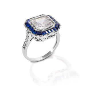 The Kelly Herd Large Asscher Cut/Blue Spinel Ring is absolutely gorgeous! The modern asscher cut is similar to an emerald cut, but larger step facets, a higher crown, and a smaller table. This combination produces more brilliance. This ring features an asscher cut clear cubic zirconia, surrounded by blue spinel. The intricate designs on sterling silver base give this ring a vintage look.  Features:      Asscher cut cubic zirconia     Blue spinel     Sterling Silver